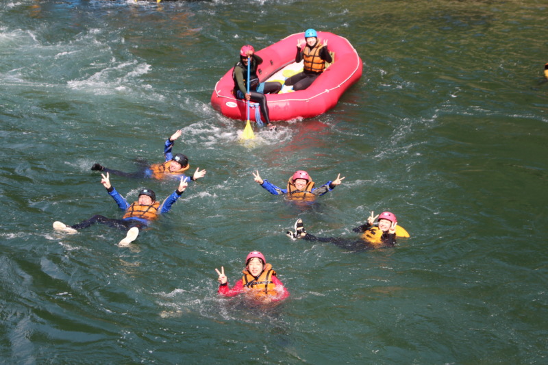 スピリットのラフティング参加者がボートの上や川の中でポーズをとるようす