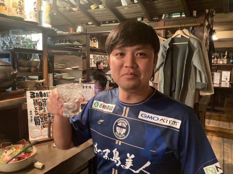 鹿児島ユナイテッドFCのユニフォームを着てお酒を飲む男性の写真