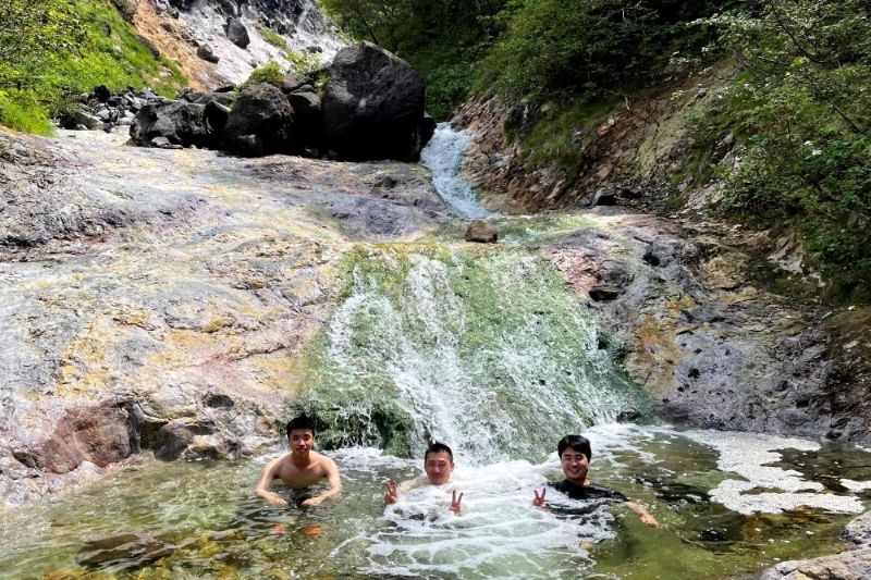 北海道の知床アルパ株式会社でカムイワッカ湯に入る男性グループ